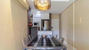 Un comedor con una mesa, sillas, una araña y una cocina al fondo.