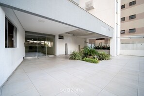 A modern building entrance with a glass door, a covered area, and a small garden with plants. - Apt Floripa, 50m to the Beach - Pad0103 (Florianópolis)