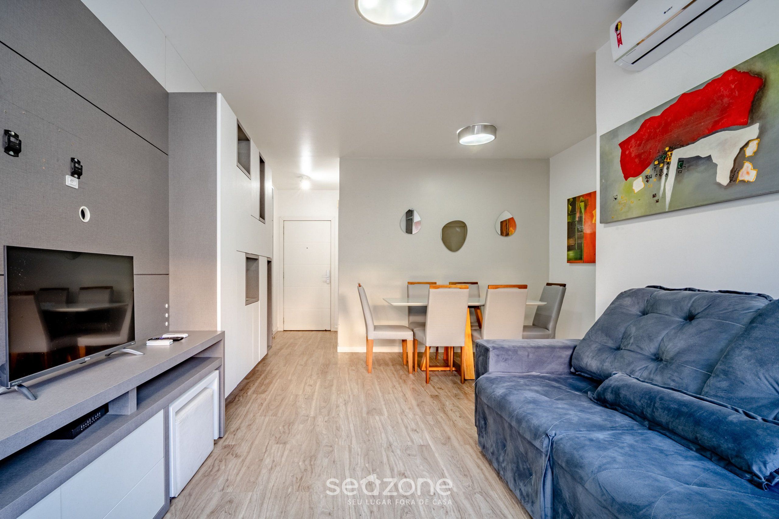 Cocina moderna con televisor integrado, zona de comedor con mesa y sillas, y sofá azul.