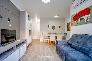 A modern kitchen with a built-in TV, dining area with a table and chairs, and a blue sofa. - Apt Floripa, 50m to the Beach - Pad0103 (Florianópolis)