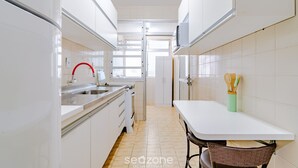 A narrow kitchen with white cabinets, a stainless steel sink, and a small dining table with a chair. - Apt Floripa, 50m to the Beach - Pad0103 (Florianópolis)