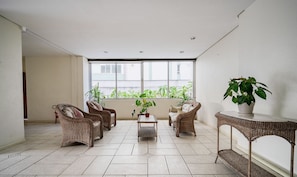 A spacious balcony with wicker furniture, a potted plant, and a view of greenery through large windows. - Apt Floripa, 50m to the Beach - Pad0103 (Florianópolis)