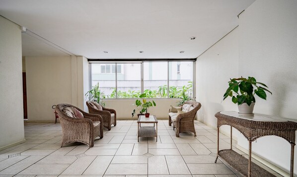A spacious balcony with wicker furniture, a potted plant, and a view of greenery through large windows. - Apt Floripa, 50m to the Beach - Pad0103 (Florianópolis)