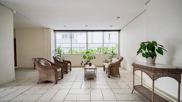 A spacious balcony with wicker furniture, a potted plant, and a view of greenery through large windows. - Apt Floripa, 50m to the Beach - Pad0103 (Florianópolis)