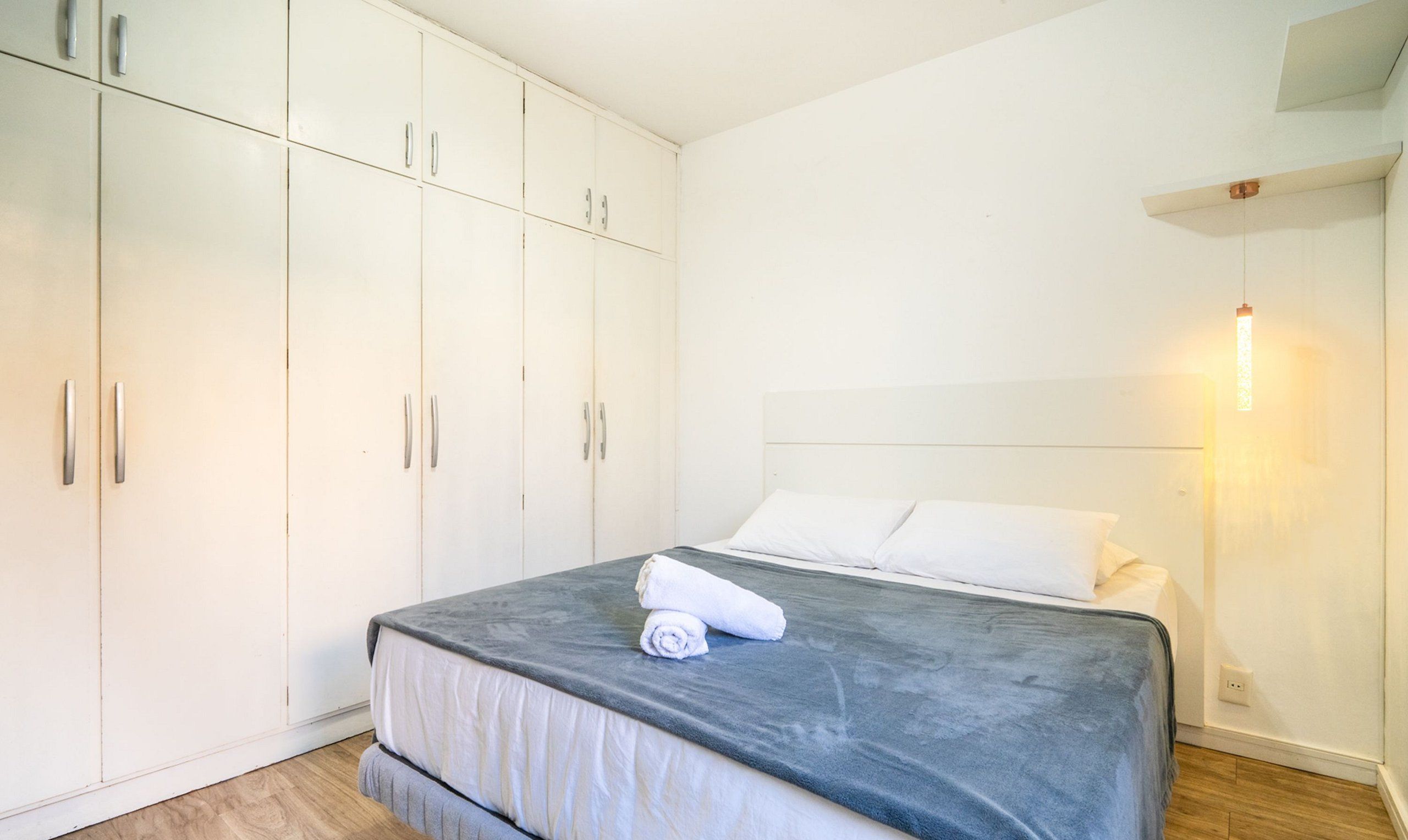 Un dormitorio con cama, armario blanco y lámpara de pared.