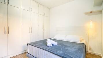 Un dormitorio con cama, armario blanco y lámpara de pared.