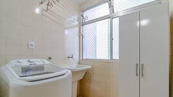 Un baño pequeño y limpio con lavadora, lavamanos y ventana con mosquitero.