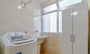 A small, clean bathroom with a washing machine, a sink, and a window with a metal screen. - Apt Floripa, 50m to the Beach - Pad0103 (Florianópolis)