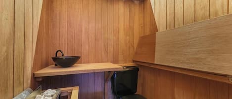A sauna room with wooden walls, a black bench, a wooden shelf, and a black basin.
