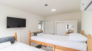 Un dormitorio con dos camas de madera, un televisor de pantalla plana montado en la pared y un equipo de aire acondicionado instalado en el techo.