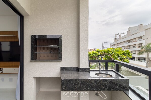 A balcony with a sink and a small shelf, a view of the city, and a building with balconies. - Apart With Barbecue 7 min From the Beach Orn0101 (Florianópolis)