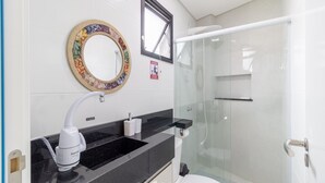 Un baño moderno con encimera negra, lavamanos blanco, espejo y cabina de ducha con mampara de vidrio.