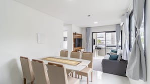 Una sala de estar moderna con comedor, sofá, televisor y balcón con cortinas.