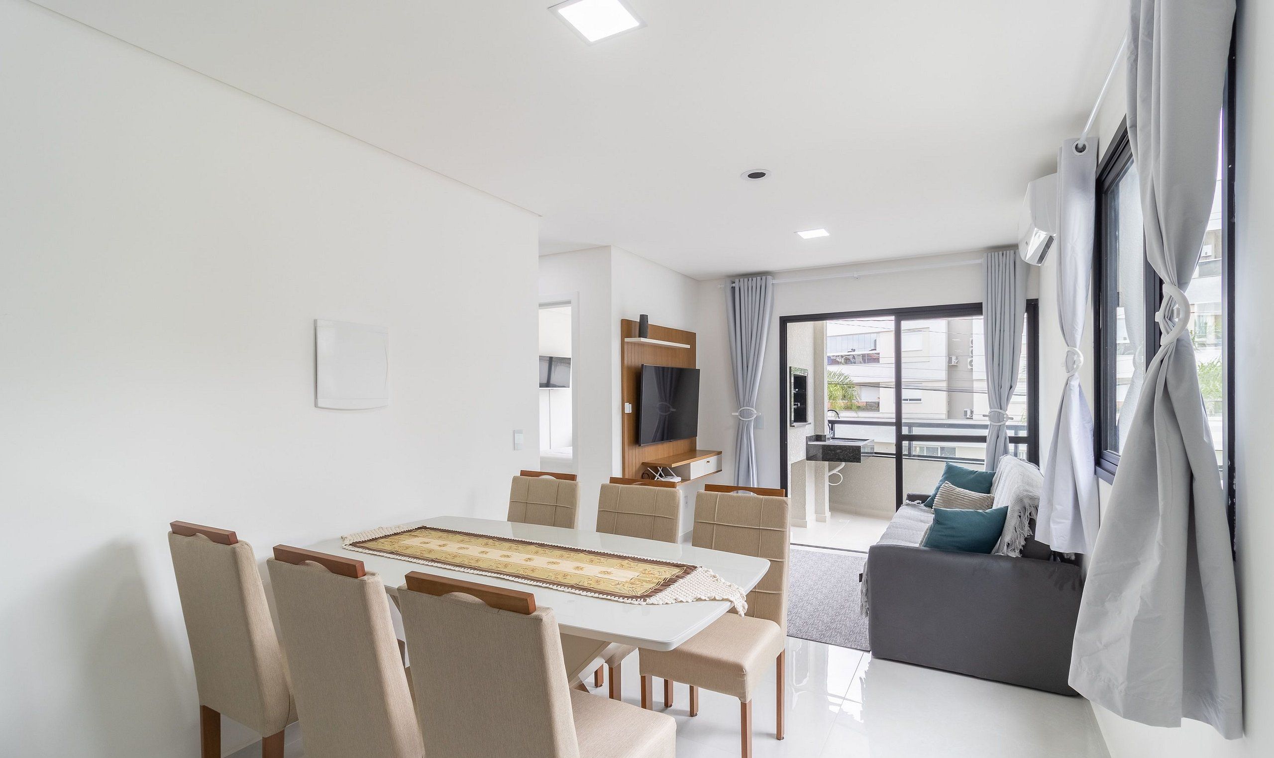 Una sala de estar moderna con comedor, sofá, televisor y balcón con cortinas.