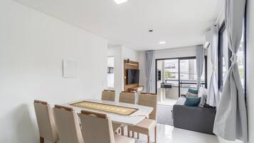 A modern living room with a dining area, a sofa, a TV, and a balcony with curtains.