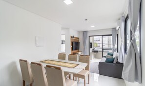 Una sala de estar moderna con comedor, sofá, televisor y balcón con cortinas.