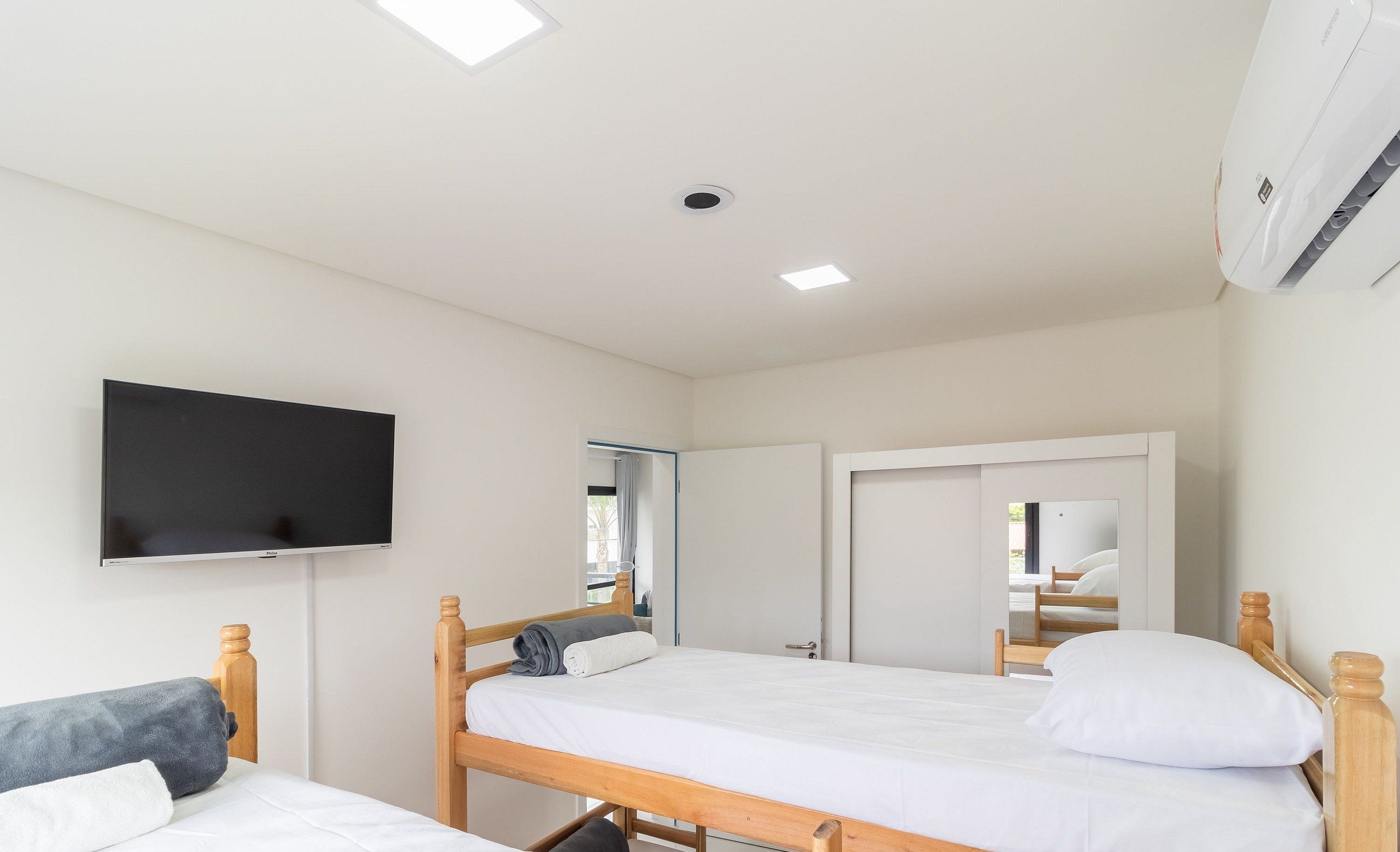 Un dormitorio con dos camas de madera, un televisor de pantalla plana montado en la pared y un equipo de aire acondicionado instalado en el techo.