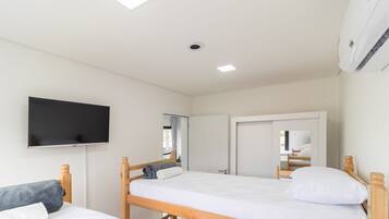 Un dormitorio con dos camas de madera, un televisor de pantalla plana montado en la pared y un equipo de aire acondicionado instalado en el techo.