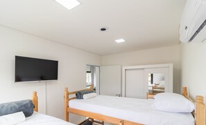 Slaapkamer met twee houten bedden, een flatscreen televisie aan de muur en een airconditioning in het plafond.