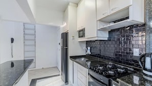 A modern kitchen with white cabinets, a black tiled backsplash, a stainless steel refrigerator, and a gas stove. - Cozy Apartment in Capoeiras, Floripa Opt504 (Florianópolis)