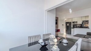 A modern dining area with a glass table, chairs, and a kitchen in the background. - Cozy Apartment in Capoeiras, Floripa Opt504 (Florianópolis)