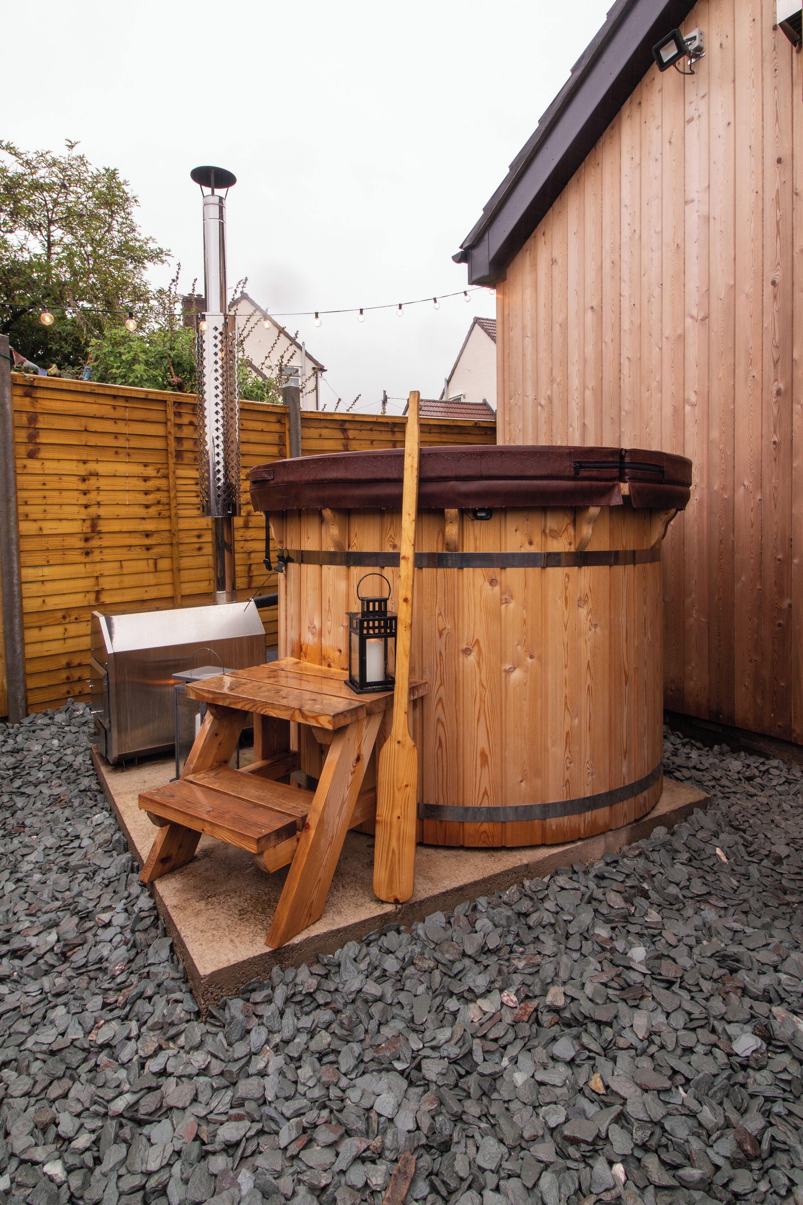 A hot tub with a wooden deck and a barbecue grill in a backyard setting.