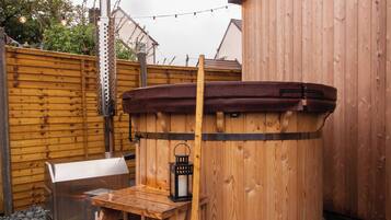 A hot tub with a wooden deck and a barbecue grill in a backyard setting.