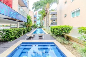 A swimming pool with lounge chairs, surrounded by greenery and modern buildings. - Beautiful Apart w/ Balcony 500m From Beach Nng0102 (Florianópolis)
