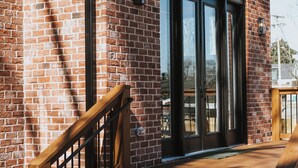 Un bâtiment en briques doté d’une terrasse en bois et d’une porte vitrée à cadre noir.