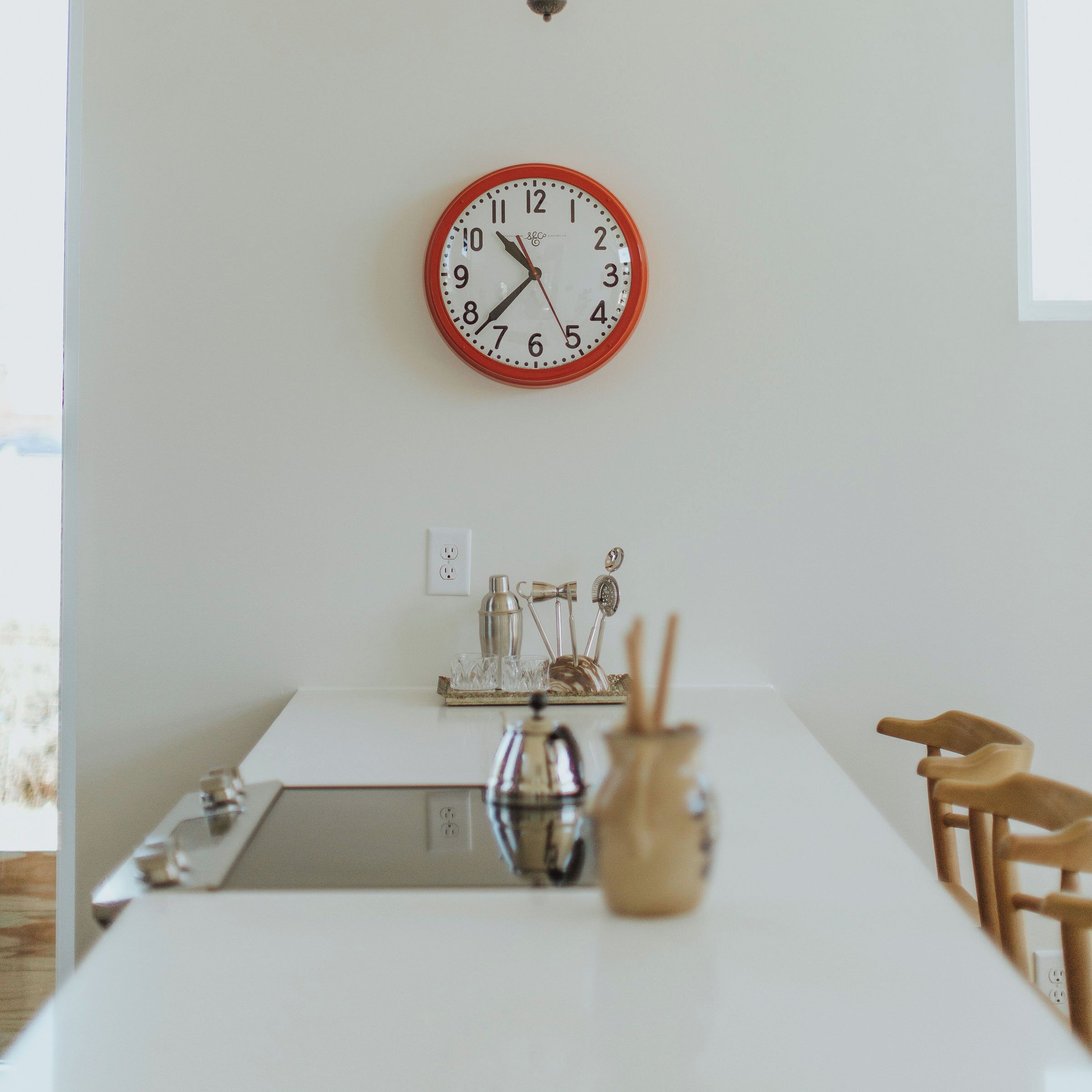Une cuisine avec un plan de travail blanc, une horloge au mur et une fenêtre.