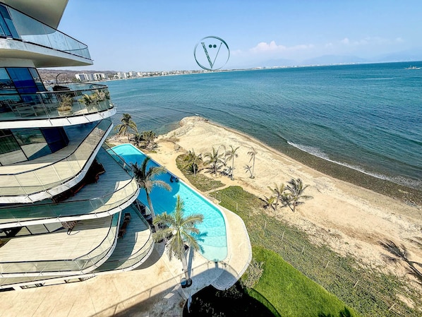 A modern building with a pool, a beach, and a clear view of the sea.