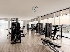 A gym with various exercise machines, large windows, and a view of the city.