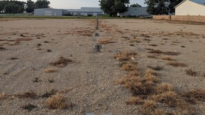 A gravel parking area with utility boxes and a large tree in the background. - Next Door to the Fair RV Park (Spencer)