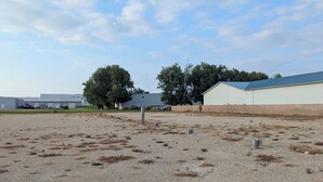 A gravel parking area with industrial buildings in the background. - Next Door to the Fair RV Park (Spencer)