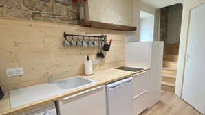 A compact kitchen with a stone wall, wooden countertop, white appliances, and a washing machine. - The House of Evahlia (Creissels)