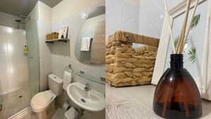 A bathroom with a glass shower enclosure, a toilet, a sink, and a mirror. There is a wicker basket on a shelf and a bottle of reed diffuser.