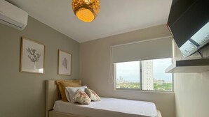 A bedroom with a bed, a window with a view of buildings, and two framed pictures on the wall.