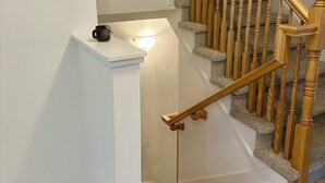 Una escalera con balaustres de madera, barandilla, peldaños alfombrados y una lámpara en la pared.