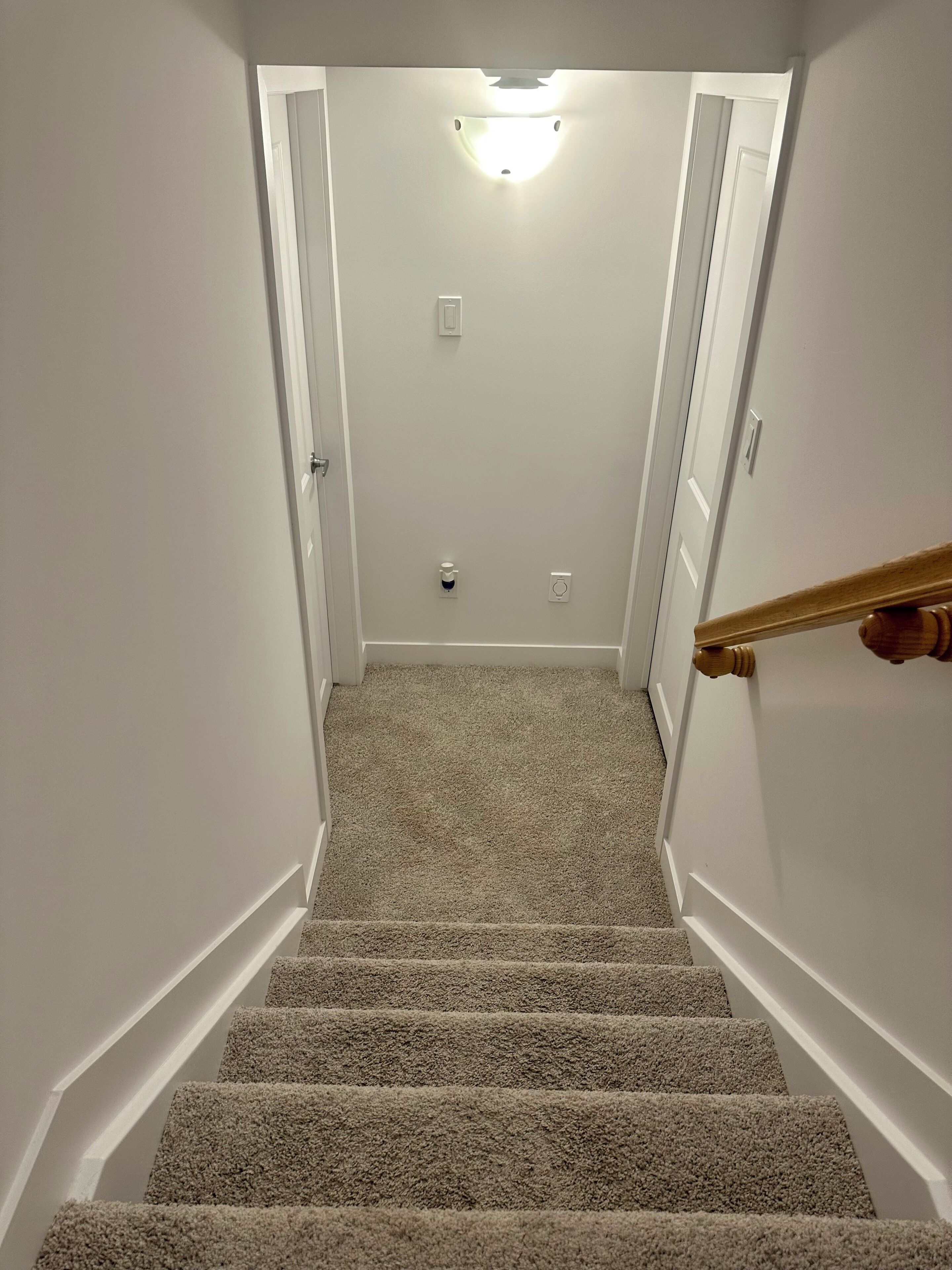 A carpeted staircase with white walls and a light fixture at the top.