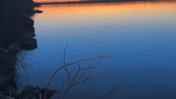 Un lago tranquilo al atardecer con una orilla rocosa y ramas desnudas en primer plano.