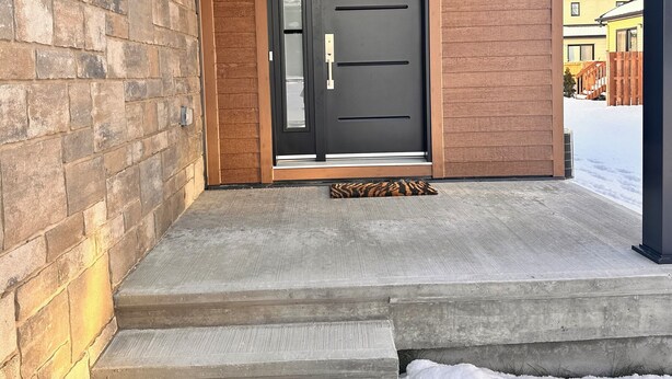 Una entrada de casa moderna con puerta negra, paredes de piedra y madera, y un porche de concreto.