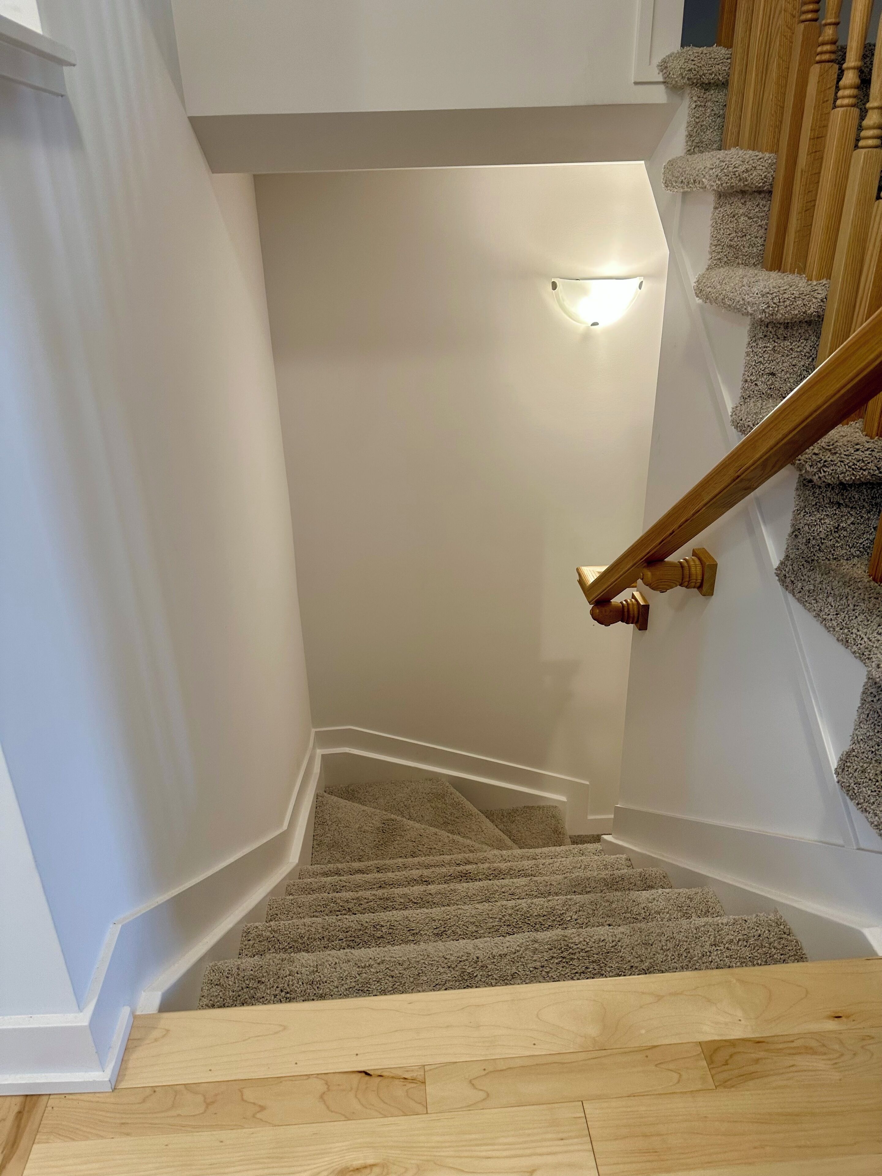 Een betegeld trappenhuis met houten leuning en een lamp erboven.