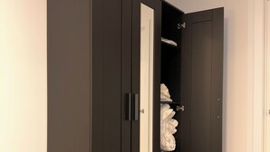 Un armario de color oscuro con puerta de espejo, una puerta blanca y un estante pequeño con ropa doblada.
