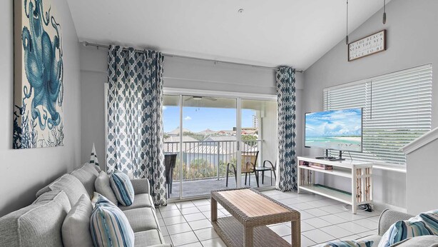 Una sala de estar con sofá, una mesa de centro, televisor y un balcón con vista a la playa.