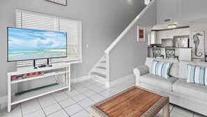 Una sala de estar con un televisor sobre un mueble bajo, un sofá, una mesa de centro y una escalera.
