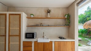 Eine moderne Küche mit Holzausstattung, einem weißen Spülbecken und einer Mikrowelle. Regale mit Pflanzen und Küchenutensilien sind ebenfalls vorhanden.