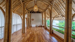 A spacious bamboo-roofed corridor with a wooden floor, white curtains, and a hanging light fixture. - Totem Bali Surf and Yoga (Jimbaran)