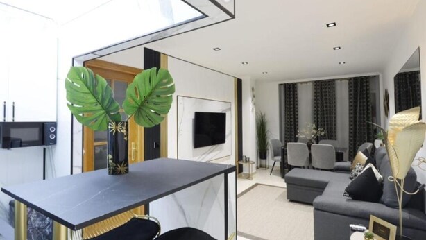Una sala de estar moderna con un sofá negro, un comedor con una mesa y sillas, y un ventanal que proporciona luz natural.