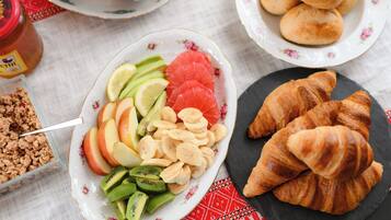 Una escena de desayuno con un plato de frutas y nueces en rodajas, un plato de croissants y un frasco de mermeladas.