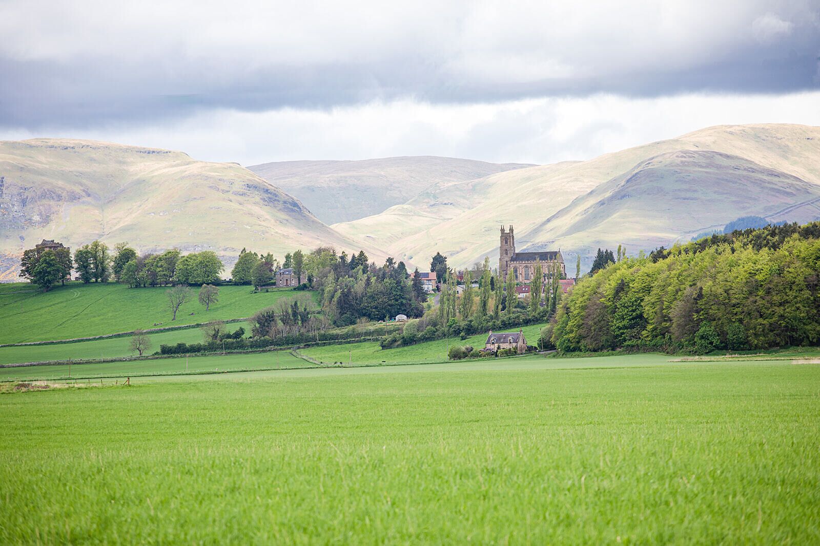 Paisaje rural con colinas onduladas, una iglesia y una pequeña casa rodeada de vegetación.